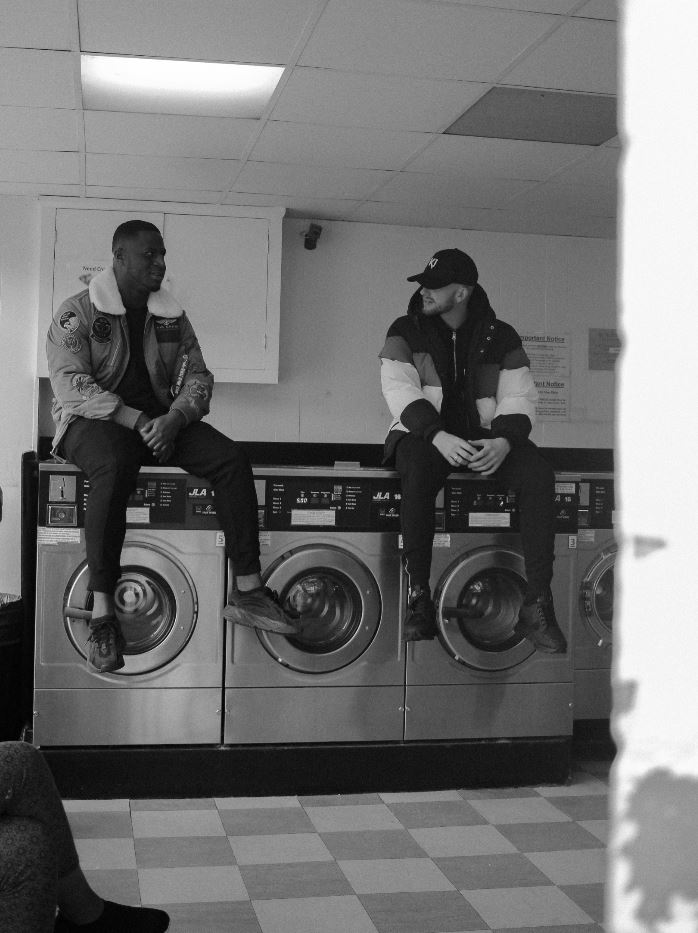 Image: Two men sitting on top of washing machines in a Coventry launderette. Image credit: HKD Media.